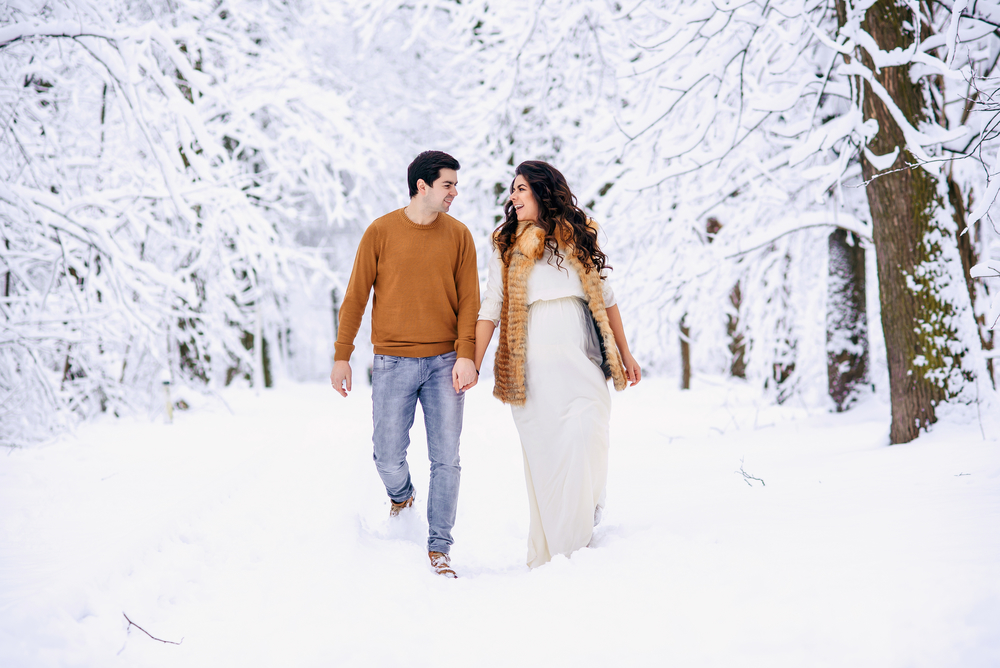 Беременная с мужем гуляют по зимней аллее на Новый год