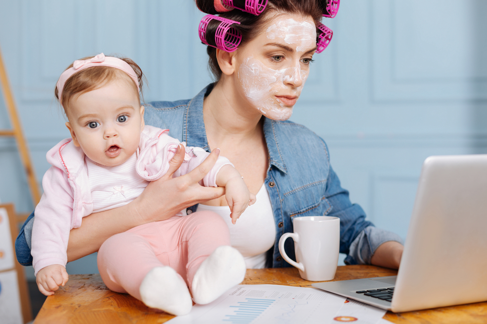 Занятая мама работает на ноутбуке с маской на лице, ребенком и чашкой кофе