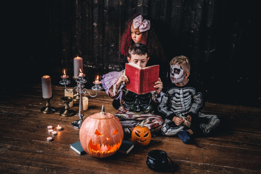 Дети в костюмах на Хэллоуин читают книгу в интерьере праздника