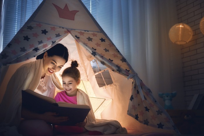 Мама с дочкой читают вечером в шалаше дома