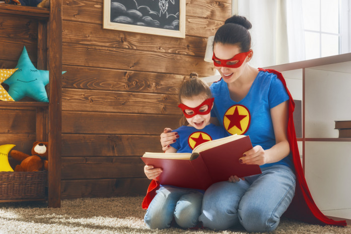 Мама с дочкой в костюмах супергероев читают книгу
