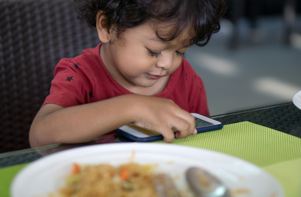 Мальчик смотрит мультики на смартфоне и не ест