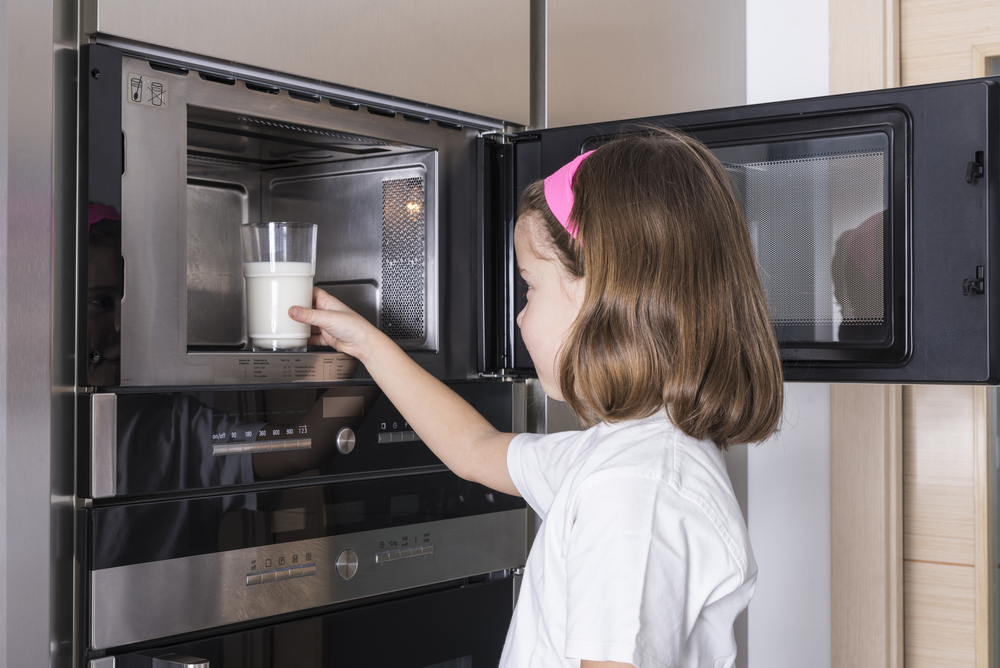 Девочка греет молоко в микроволновке
