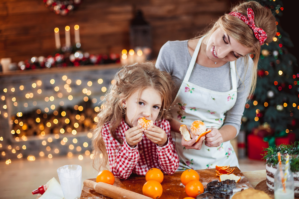 Девочка ест цитрусовые на Новый год вместе с мамой