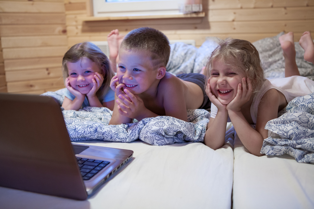 Дети смотрят мультфильмы на ноутбуке, лежа в постели