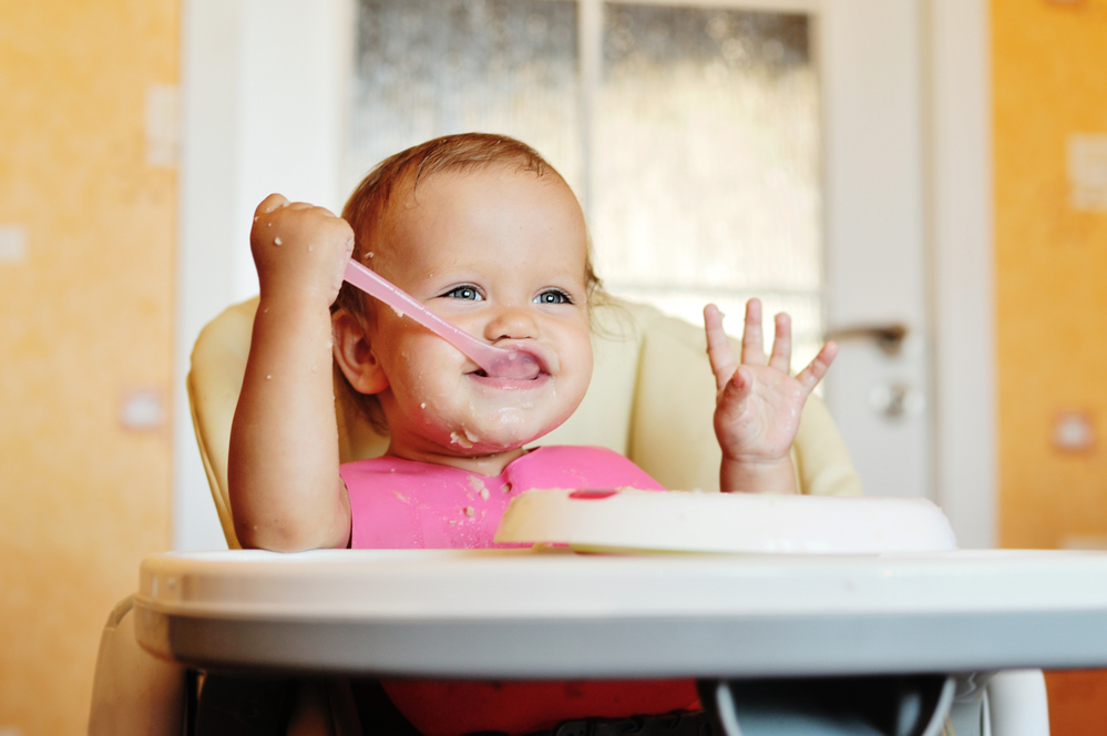 Ребенок ест ложкой в стульчике для кормления