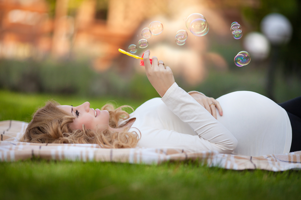 Беременная девушка расслабляется на природе, пуская мыльные пузыри