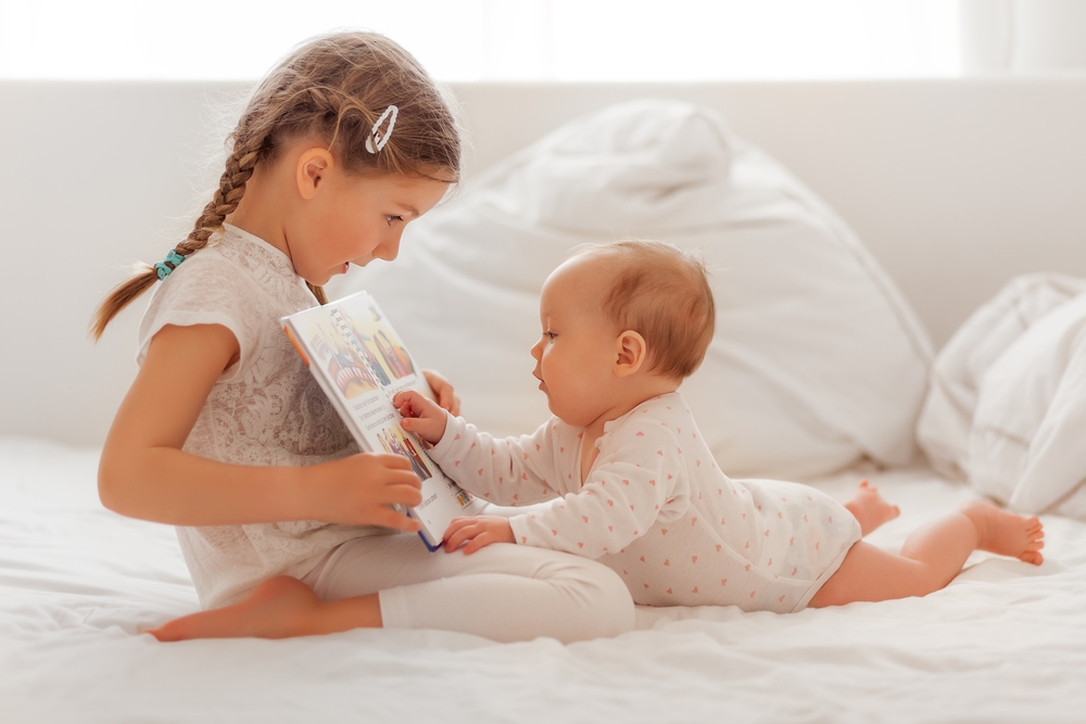 Малыш читает книжку с сестрой