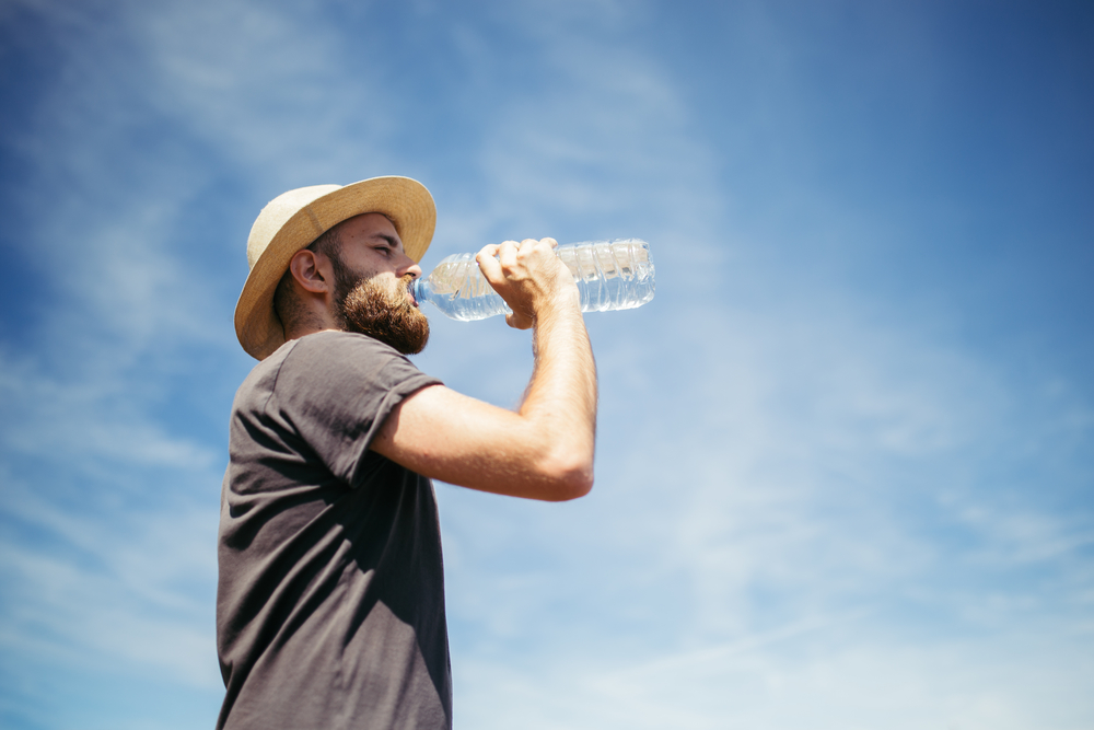 Мужчина пьет воду на фоне неба