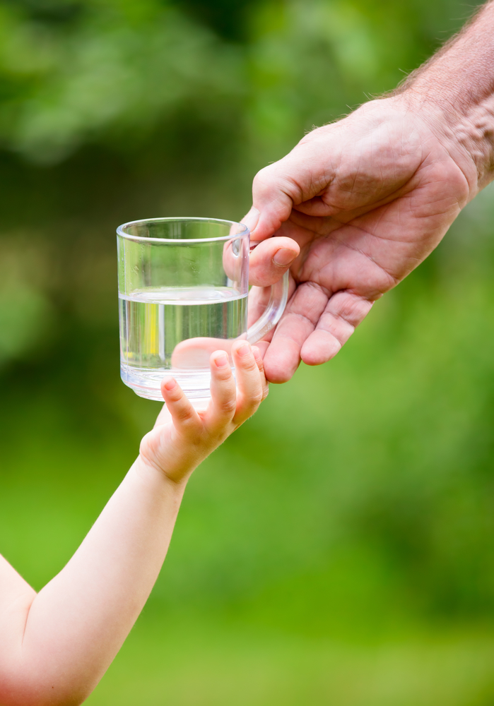 Взрослая рука дает детской руке стакан воды