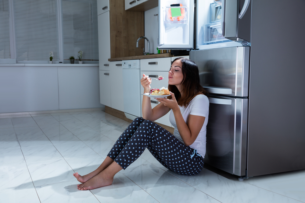 Женщина у холодильника ест сладости