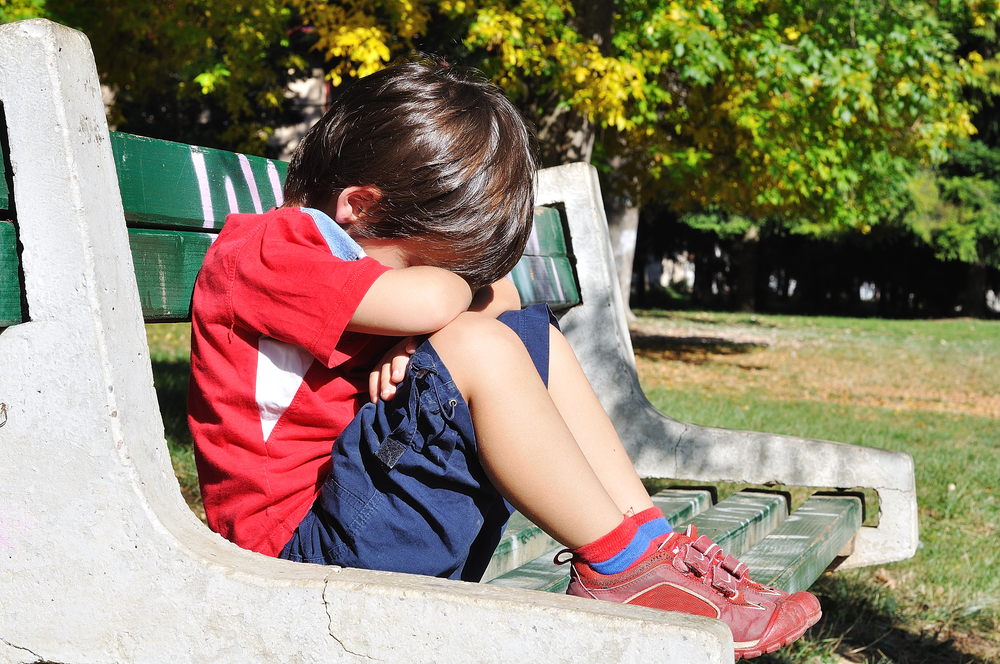 Мальчик на скамейке в парке грустит