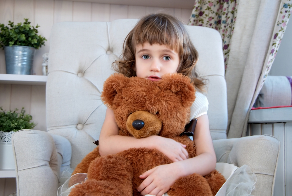 Дівчинка з ведмедиком сидить в кріслі