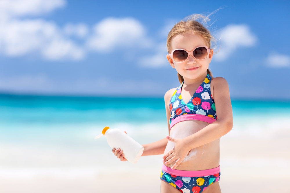 Девочка на пляже мажется солнцезащитным кремом