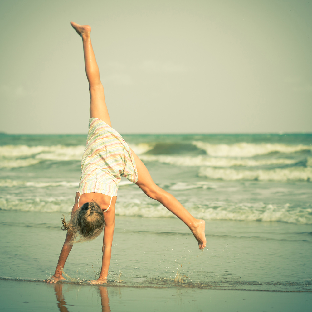 Девочка стоит на руках на пляже у моря