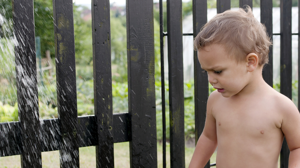 Дитина приймає душ у дворі