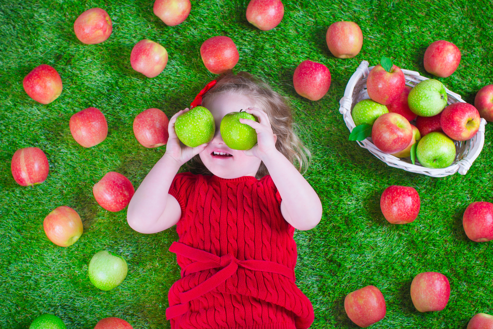 Девочка играет с яблоками на траве