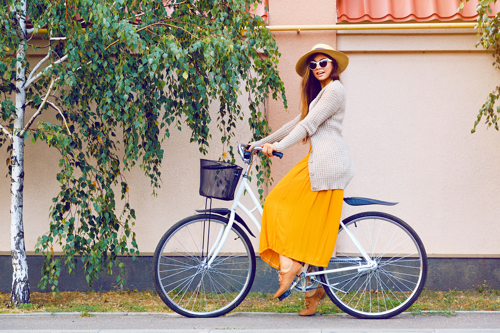 Девушка в юбке и в шляпке на велосипеде летом