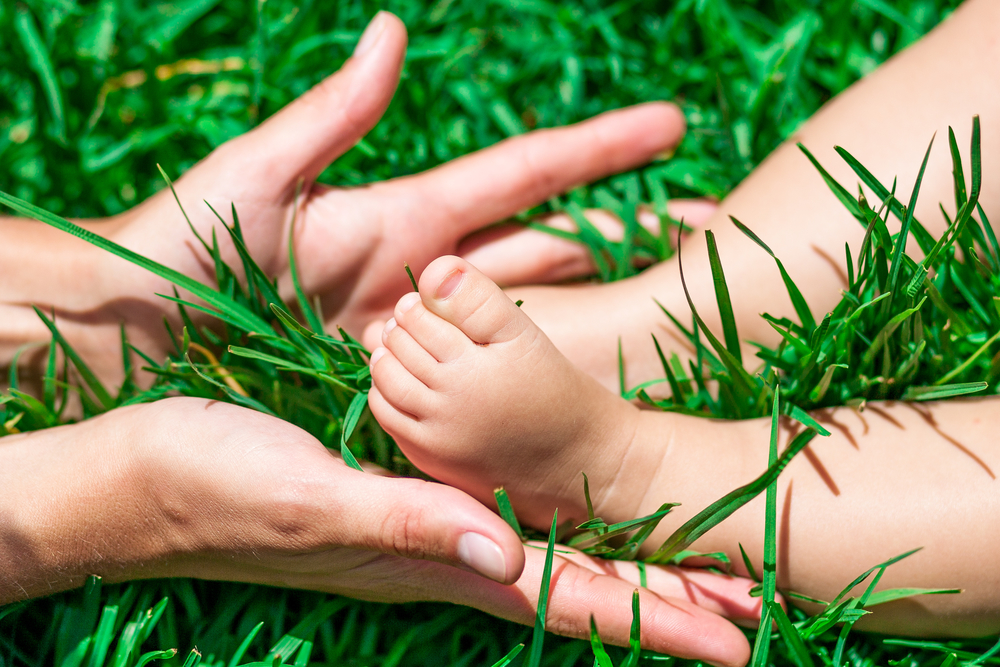 Детские ножки в маминых руках на трава - профилактика плоскостопия
