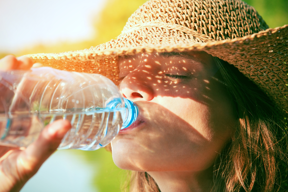 Женщина пьет воду в жару для профилактики инфаркта