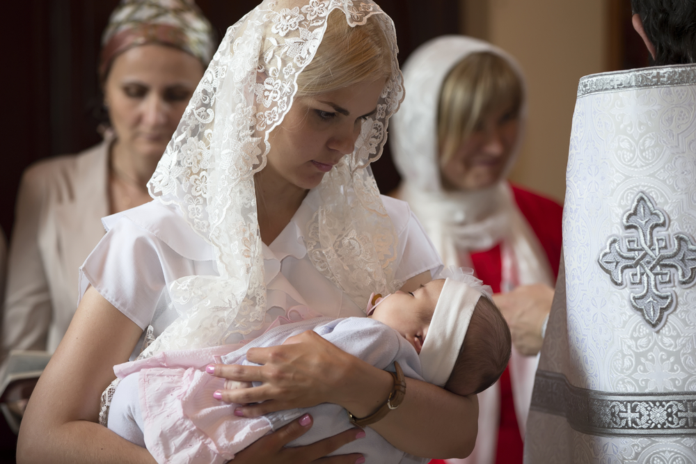 Крестная мама держит девочку в крестильной одежде