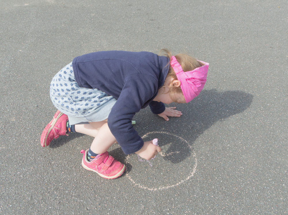 Девочка рисует круг на асфальте
