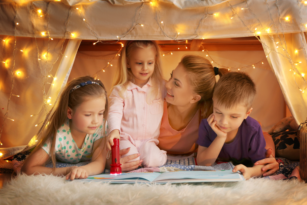 Мама с детьми читают вечером в палатке