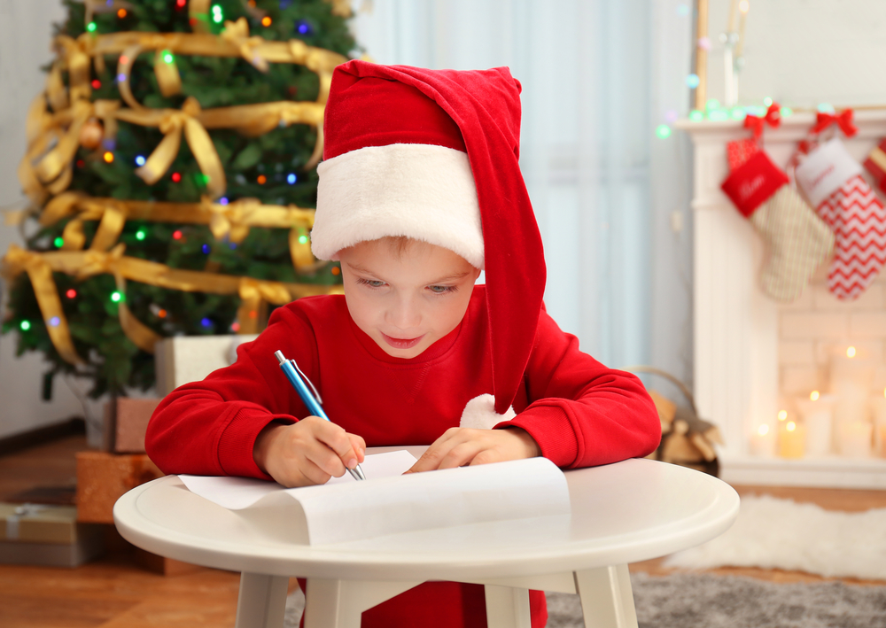 Ребенок пишет письмо святому Николаю под елкой