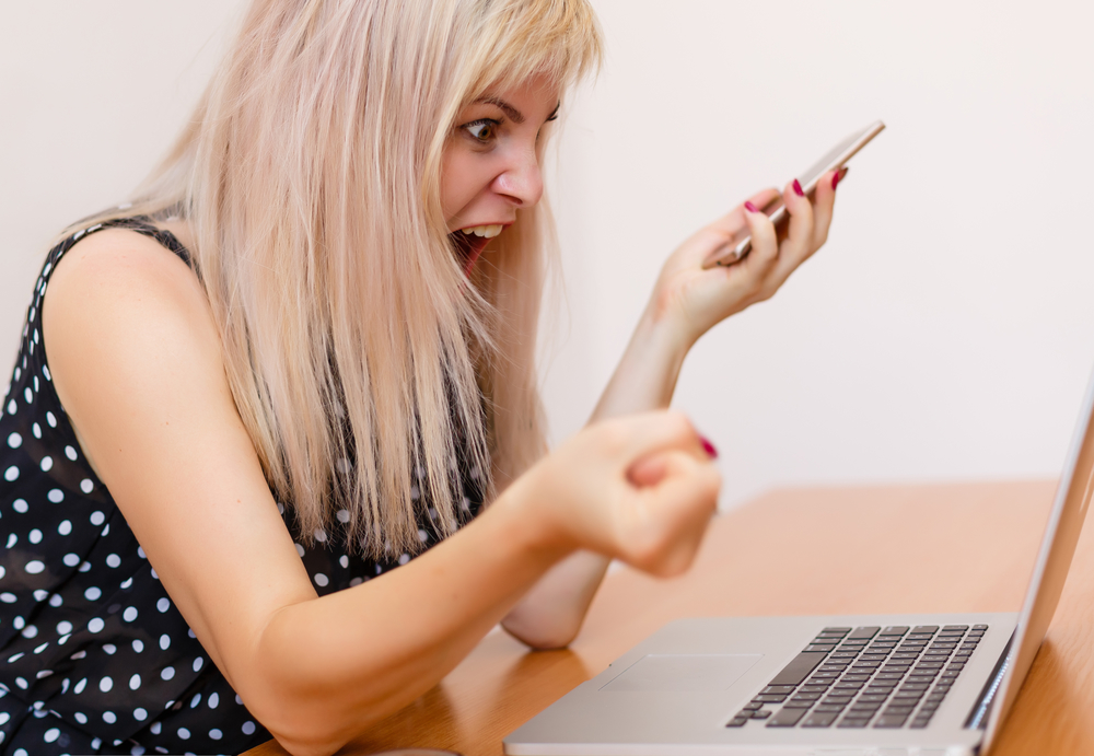 ​Засмучена жінка з телефоном кричить у ноутбука
