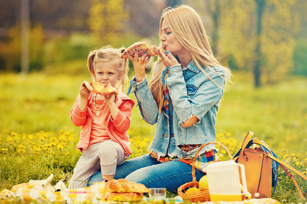 ​Мама з дівчинкою їдять піцу на пікніку