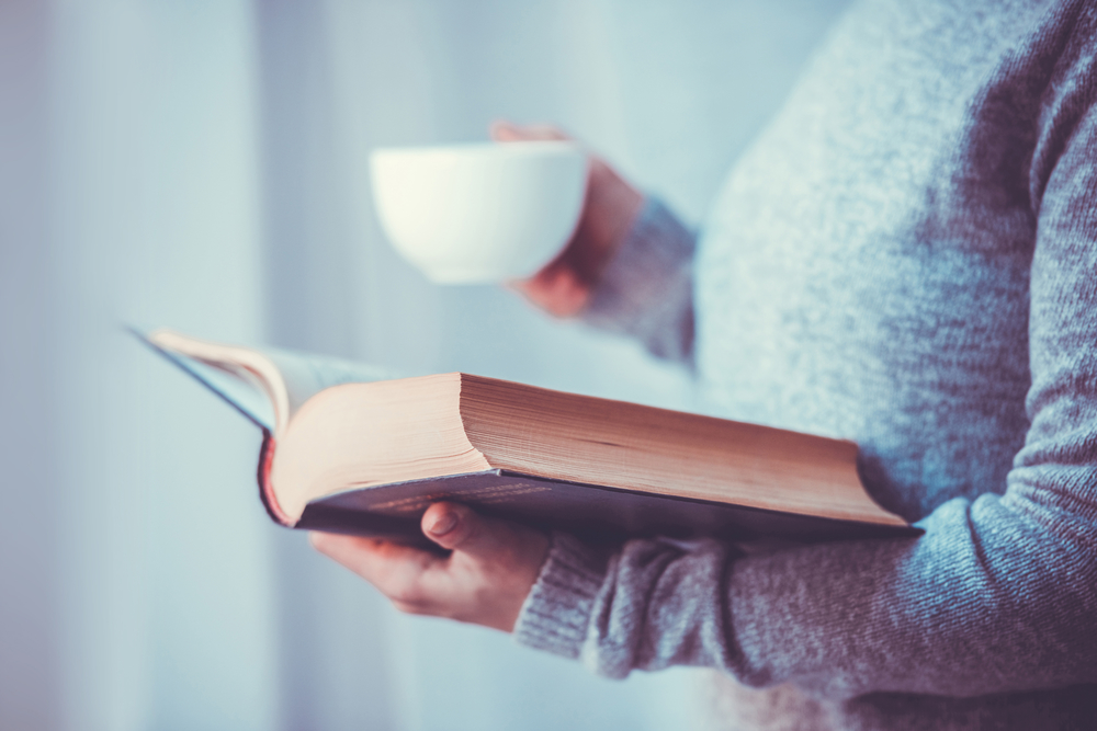 Женщина читает книгу с чашкой чая
