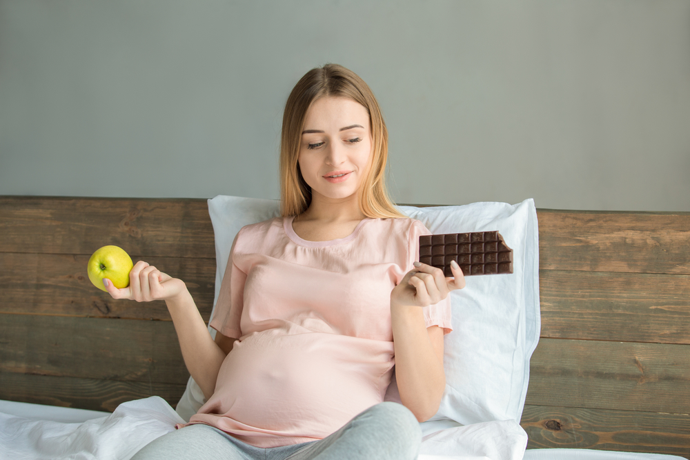 Беременная выбирает между шоколадкой и яблоком