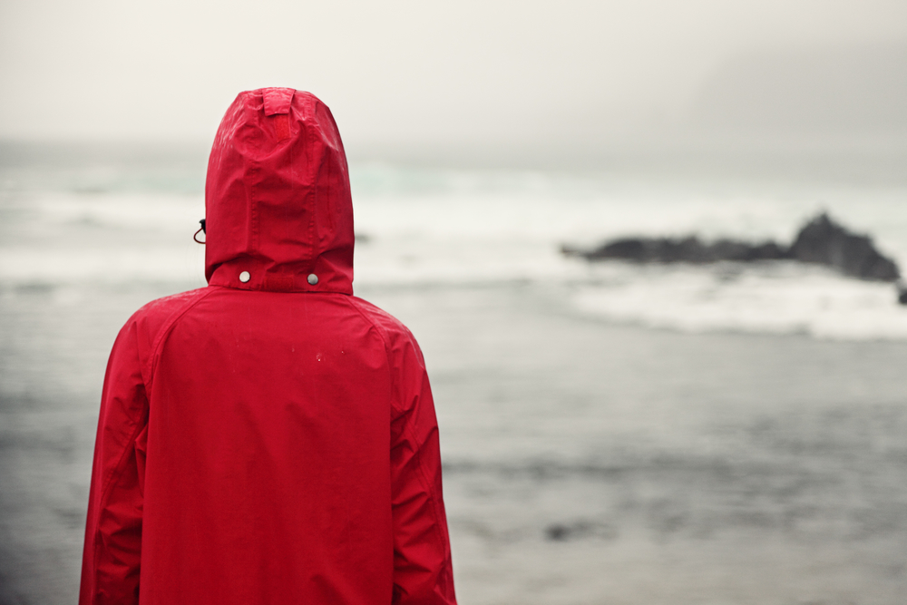 Жінка в червоній куртці на тлі сірого неба і моря - депресія