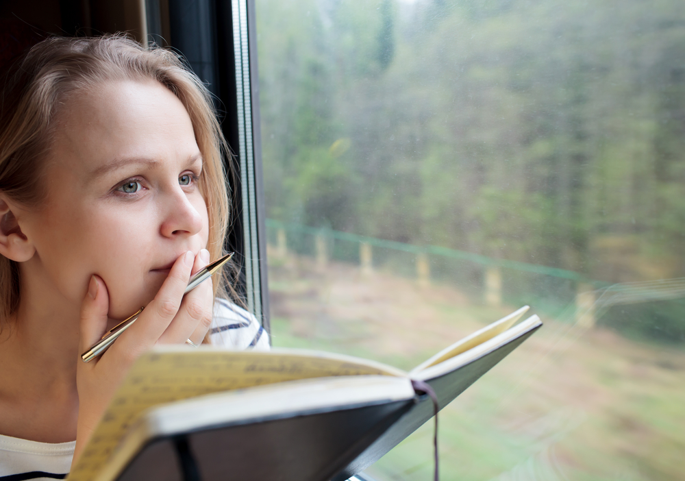 Женщина сидит у окна и пишет дневник
