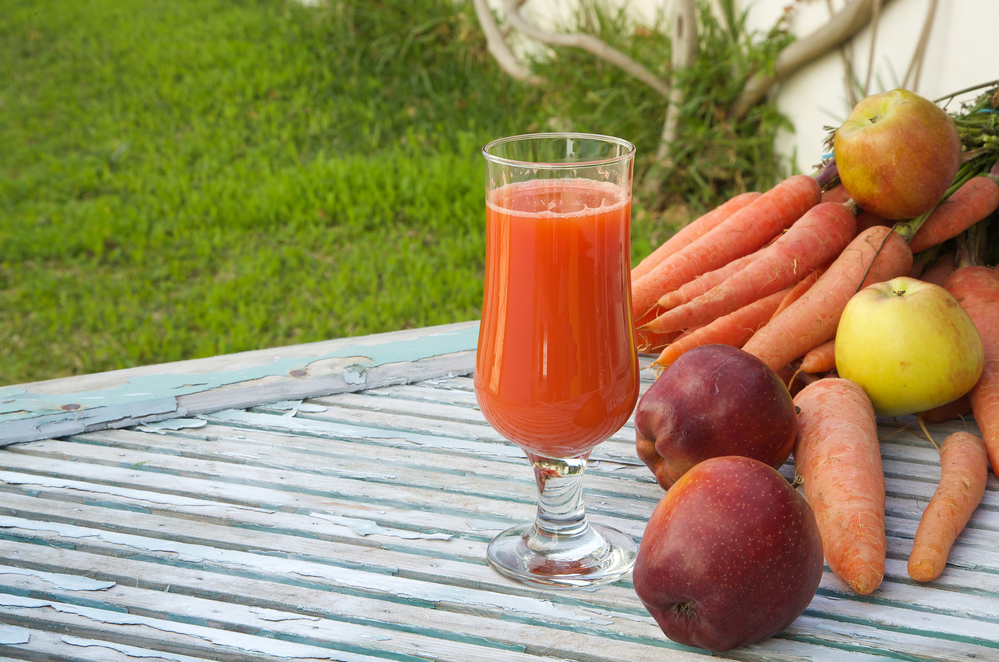 Морковка и сок фрэш на столе на фоне травы